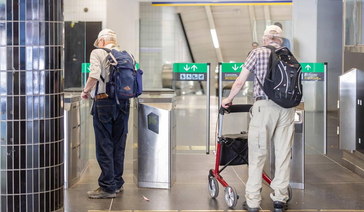 Två äldre män går genom en spärrlinje på en tunnelbanestation.
