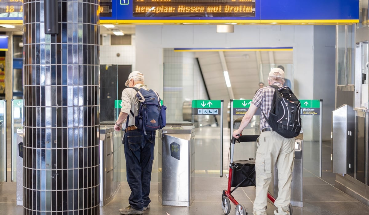 Två äldre män går genom en spärrlinje på en tunnelbanestation.