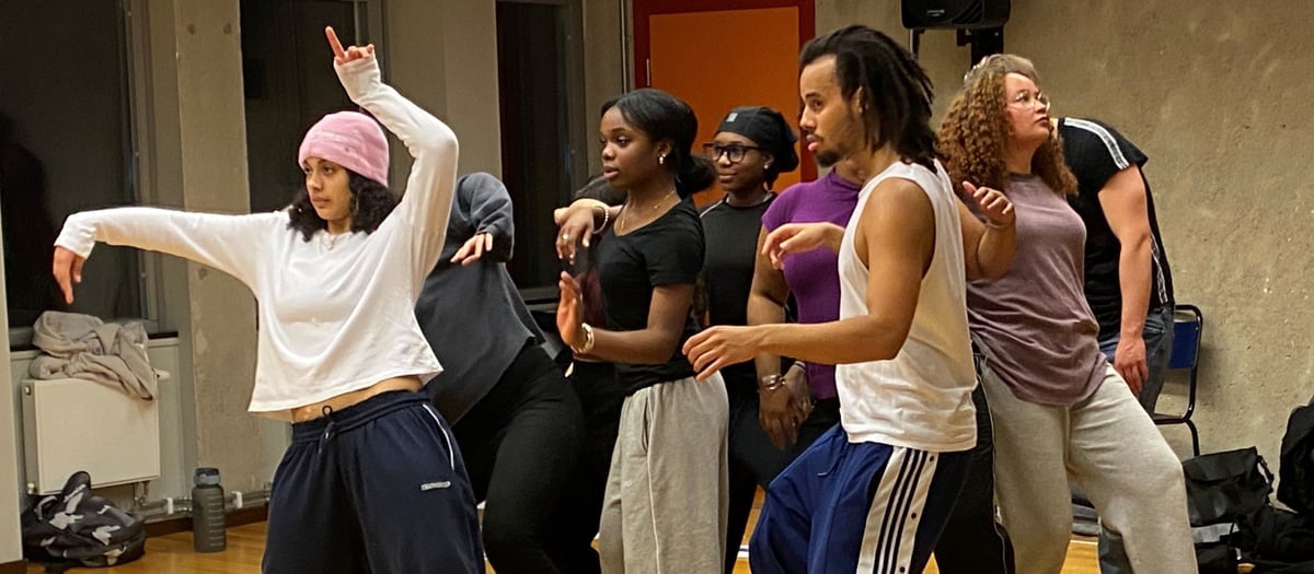 En grupp unga människor tränar dans  i en sal med trägolv.