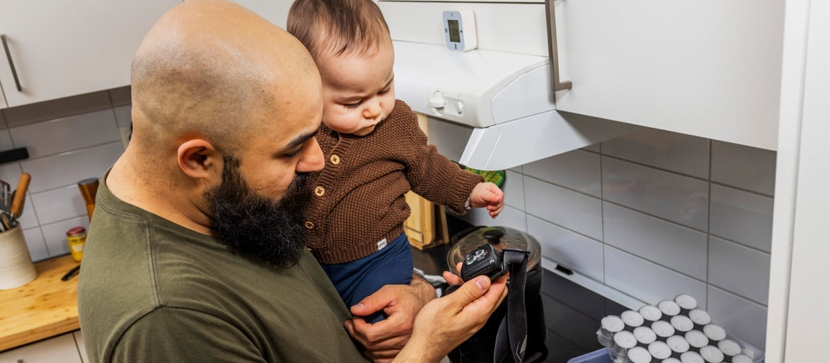 En man håller i en bebis i ett kök.