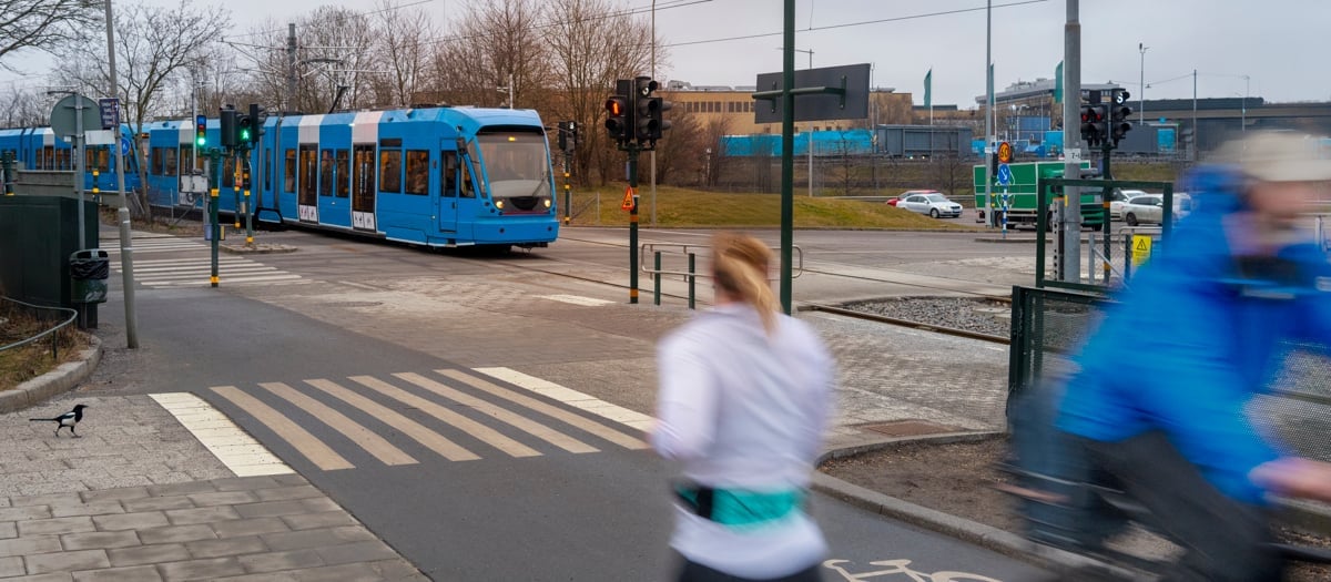En man cyklar längs en gata bredvid en blå buss.