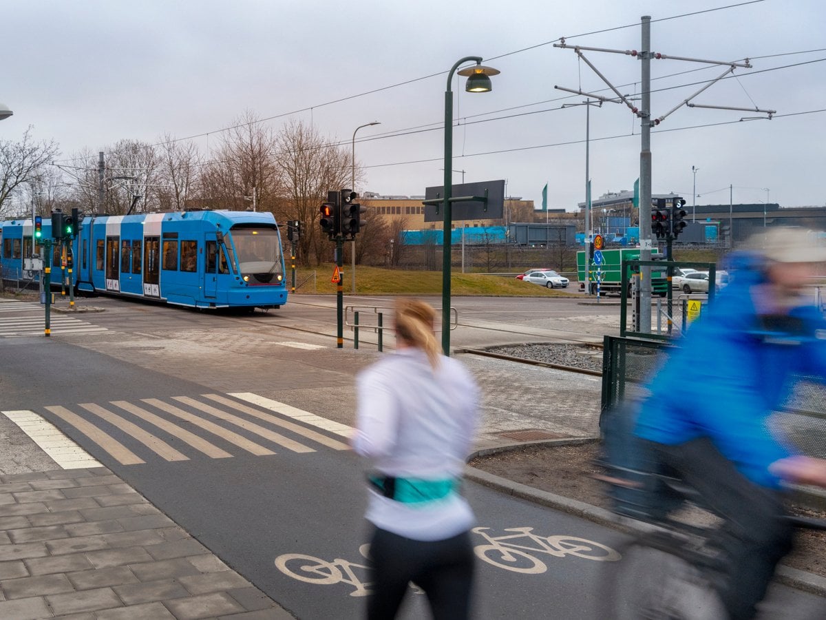 En man cyklar längs en gata bredvid en blå buss.