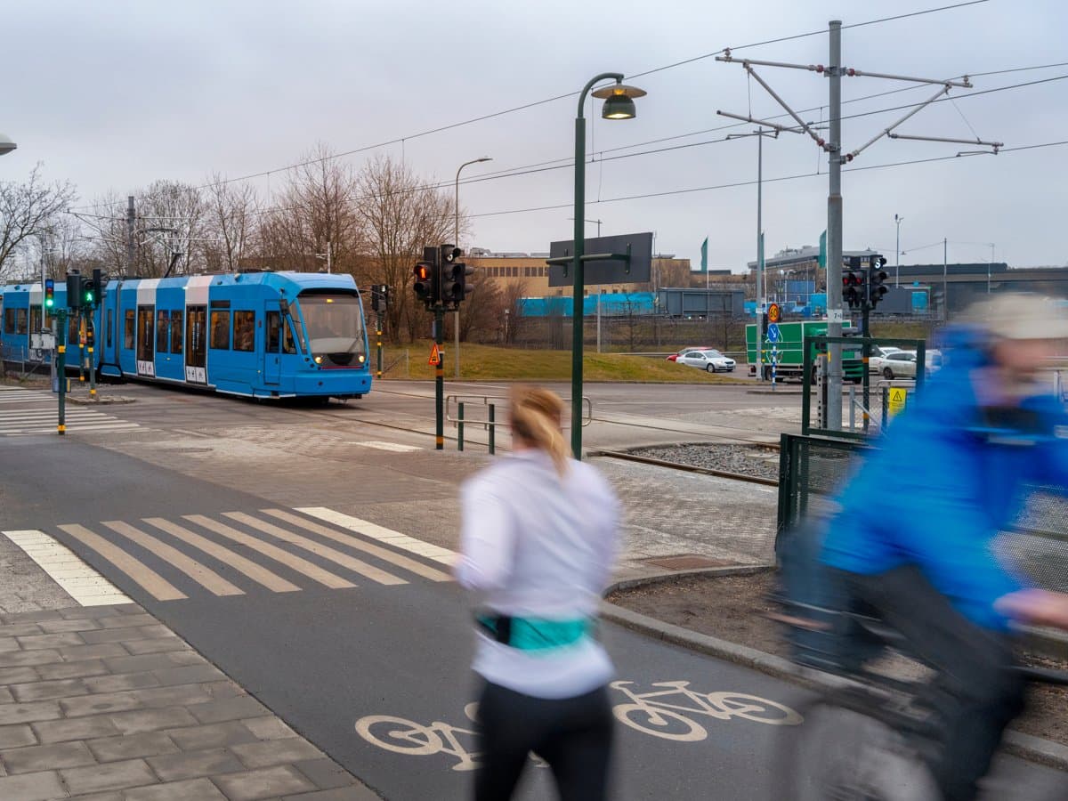 En man cyklar längs en gata bredvid en blå buss.