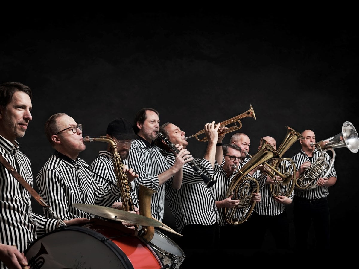 En grupp musiker med svartvitrandiga skjortor och instrument mot en svart vägg