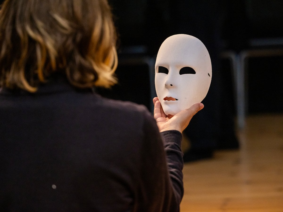 En kvinna håller en vit mask framför sitt ansikte.