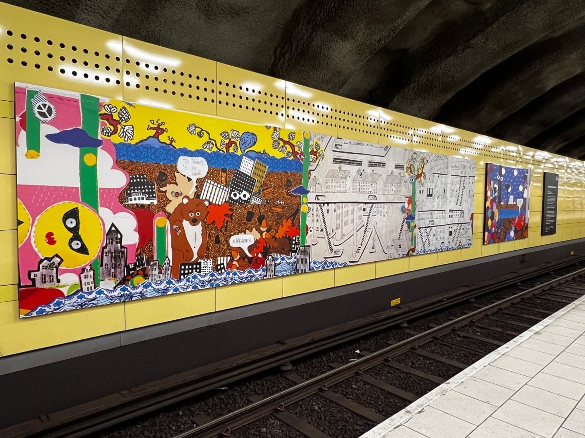 En tunnelbanestation med konsttavlor på en gul vägg.