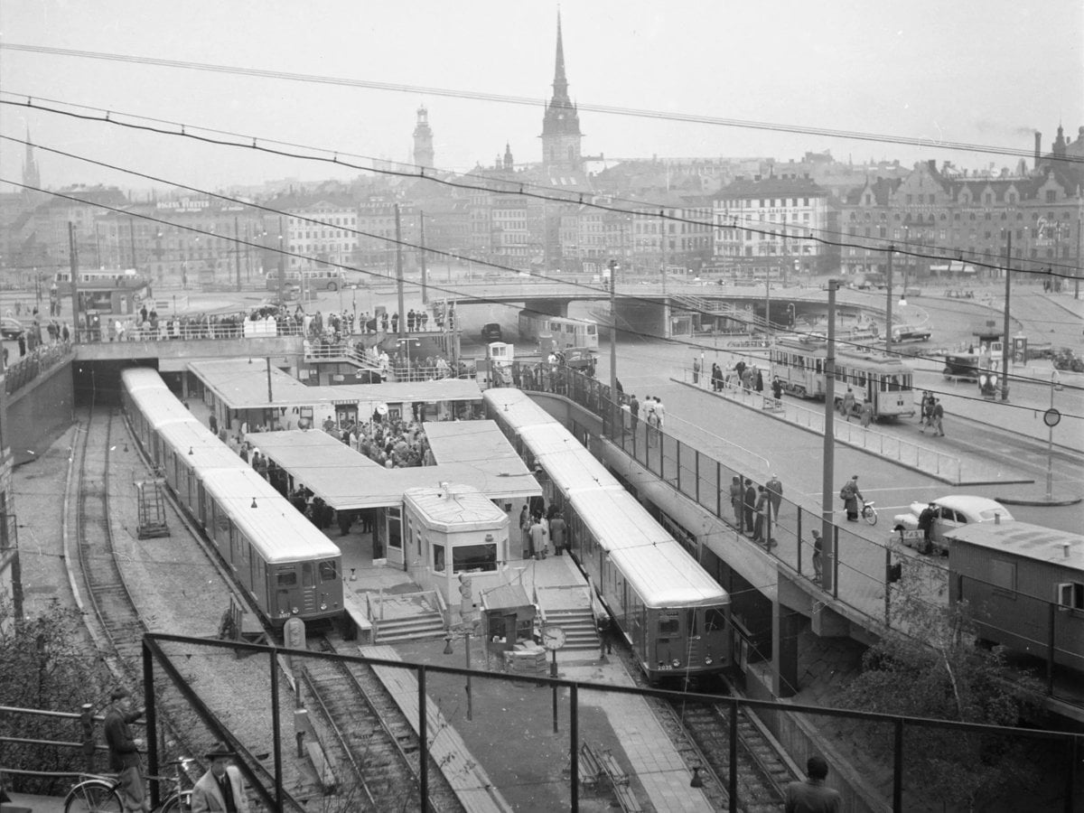 Ett svartvitt foto av invigningen av tunnelbanan 1950. Två tåg står inne på perrongen vid Slussen och fullt med människor.