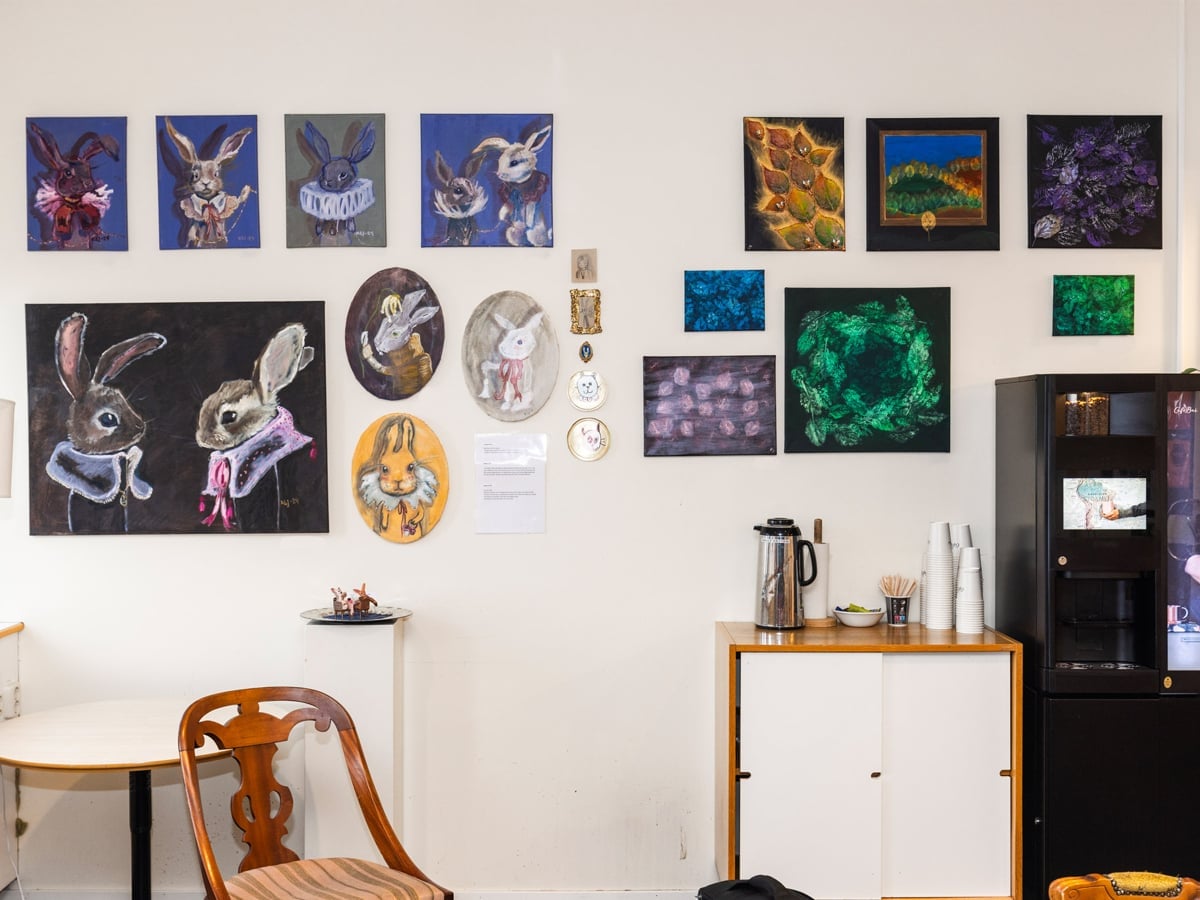 Tavlor utan ram på en vit vägg. Under tavlorna kaffeautomat.