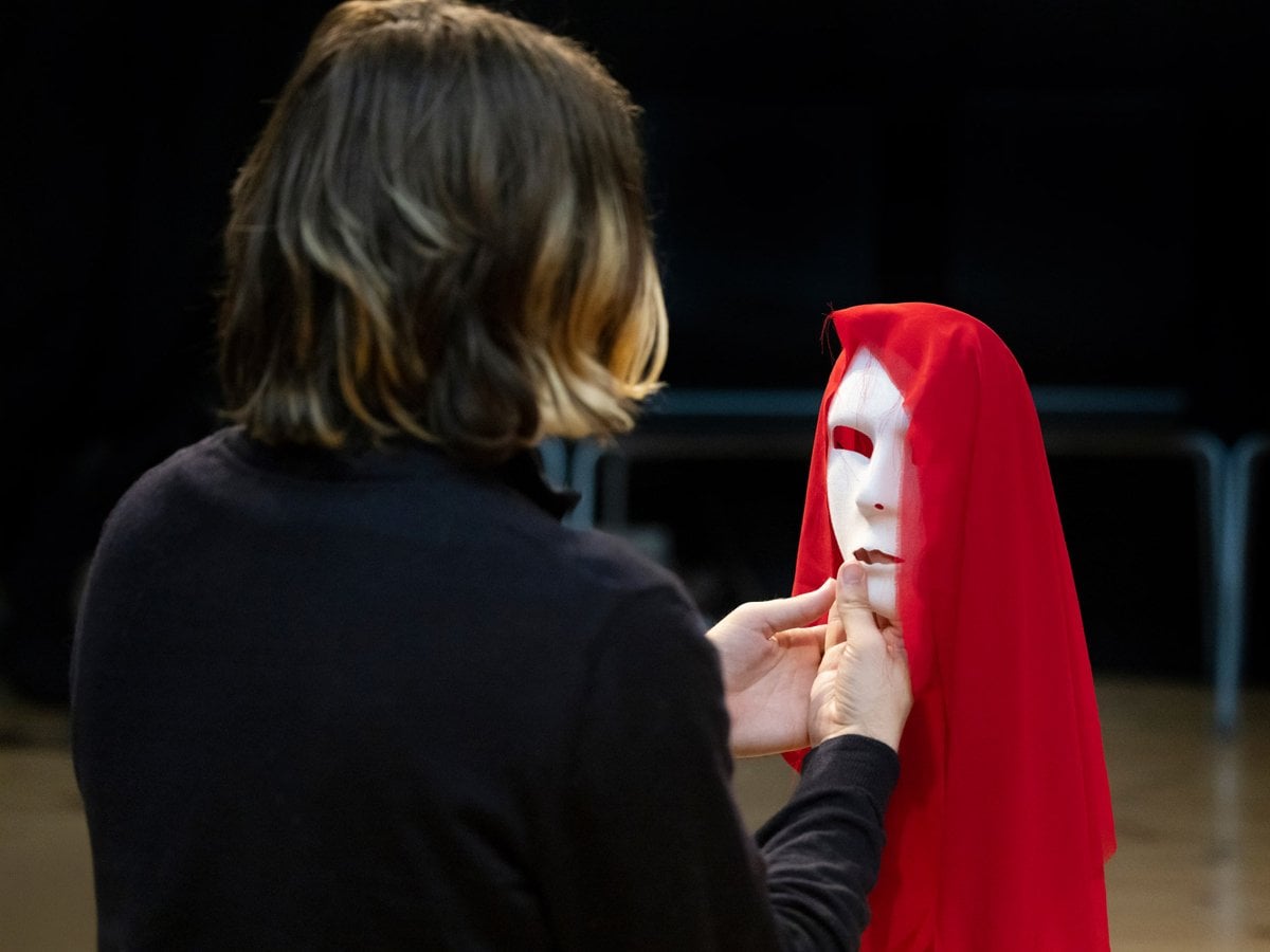 En kvinna i röd slängkappa och vit mask.