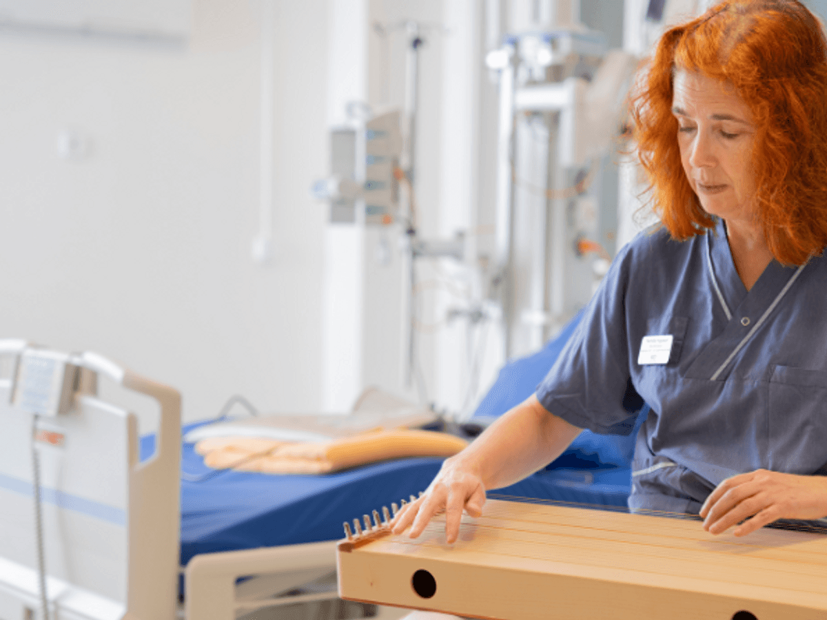 Pernilla sitter med instrument i knät. Bakom skymtar en sjukhussäng.