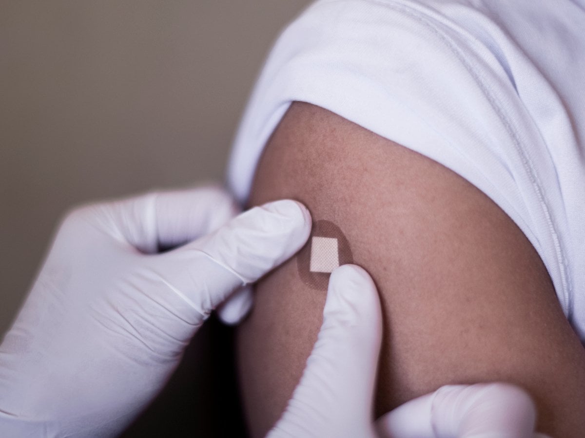 Närbild på händer med handskar som sätter på ett plåster på en arm