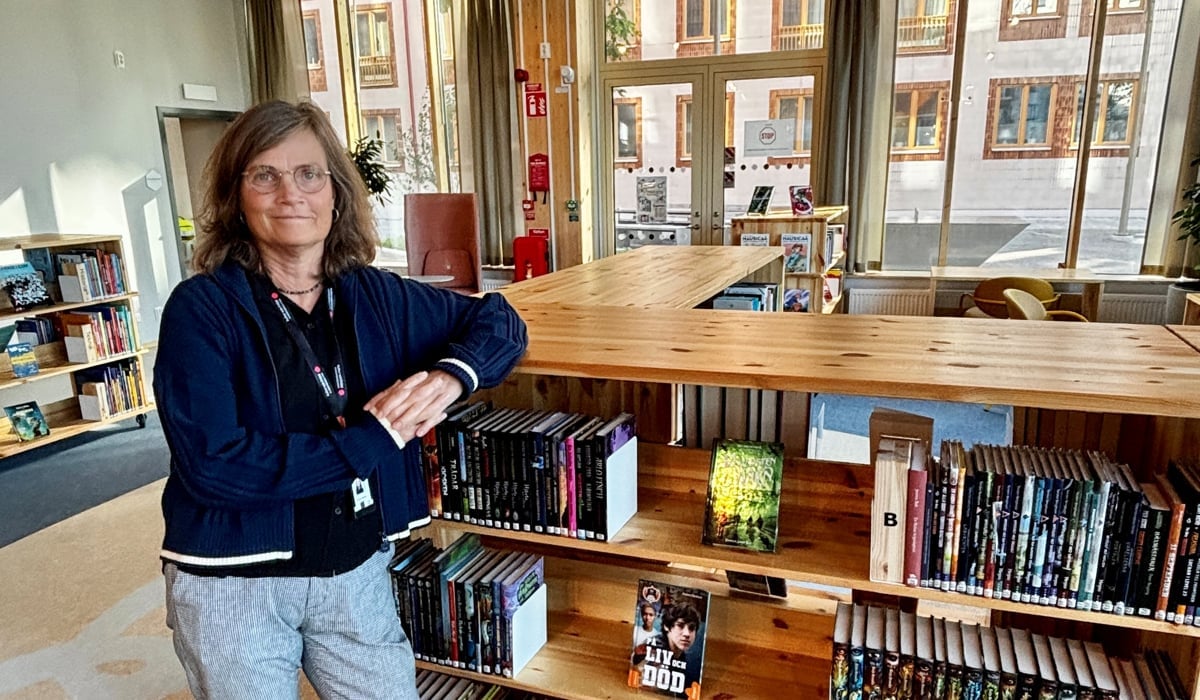 En kvinna står lutad mor en bokhylla i en biblioteksmiljö.