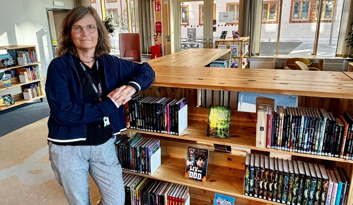 En kvinna står lutad mor en bokhylla i en biblioteksmiljö.