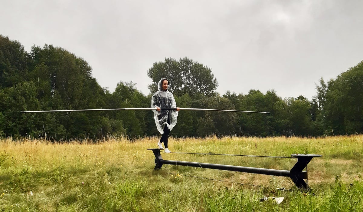 En person går på lina över ett gräsbevuxet fält med en regnponcho.