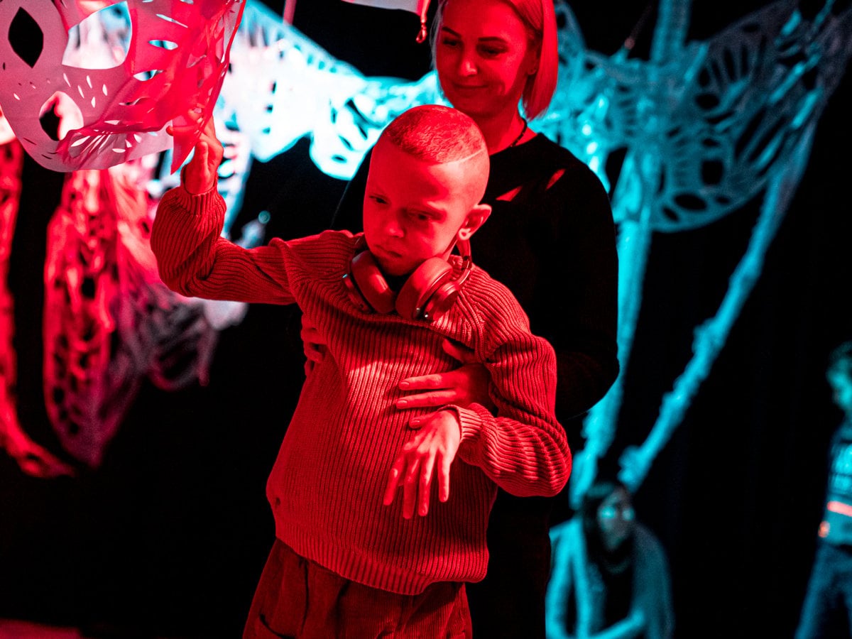 Ett barn som har svårt att röra sig rör sig med stöd av en vuxen på en scen med färgglada dekorationer