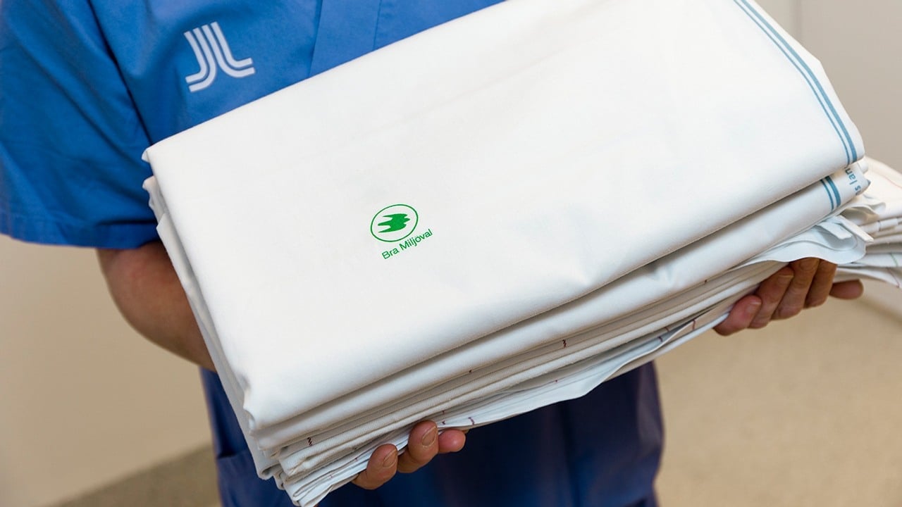 Medarbetare inom sjukvården håller i en hög med lakan med märket Bra miljöval