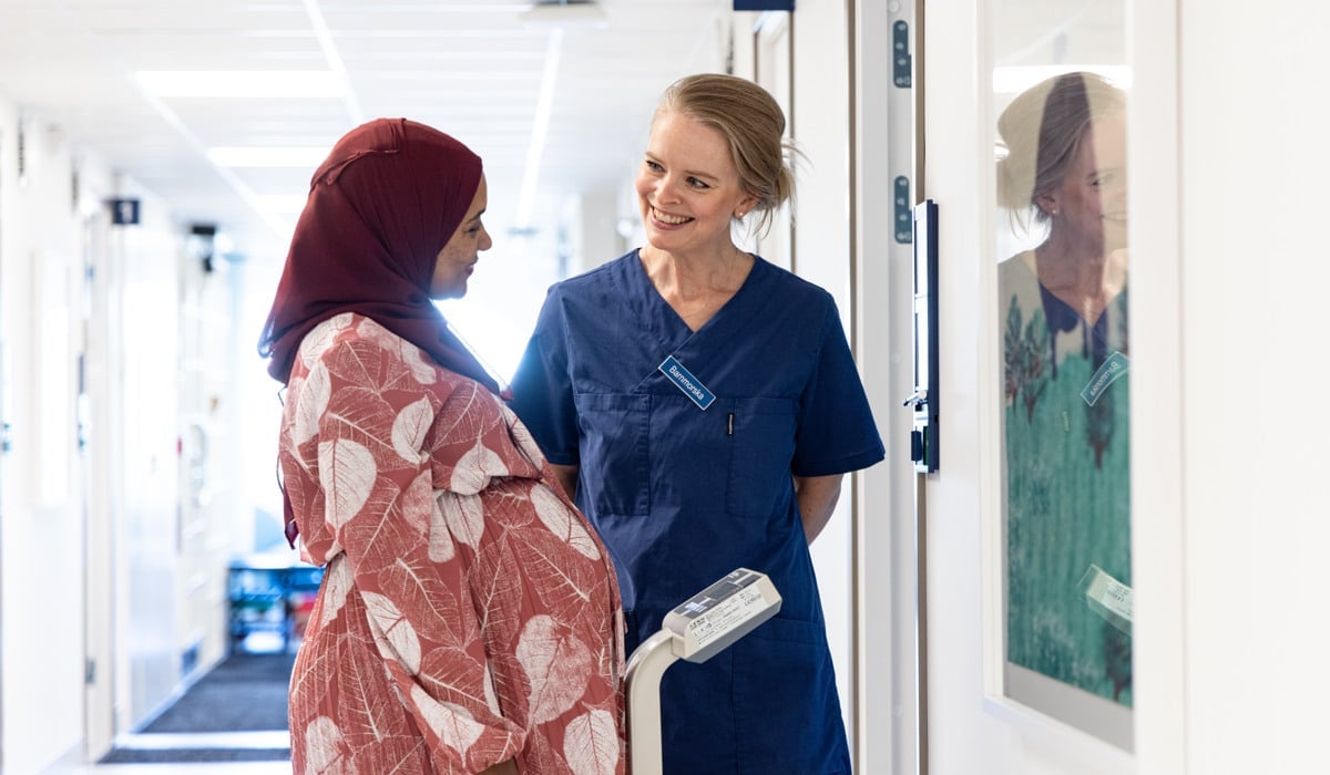 Gravid kvinna väger sig och pratar med barnmorska