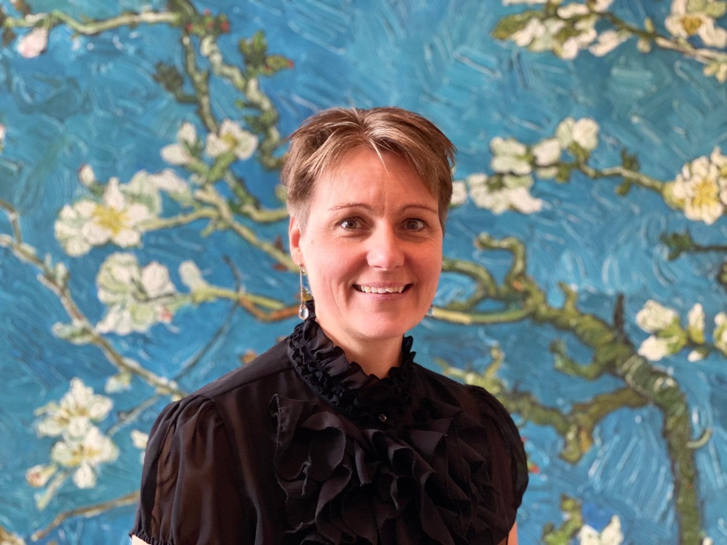 Bild på kvinna som står framför en blommig tapet.