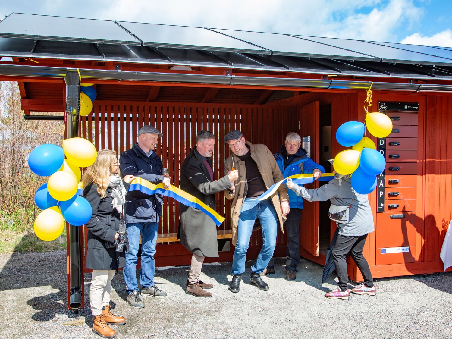 Sex personer står vid ett invingingsband omringade av ballonger. De inviger en servicebyggnad