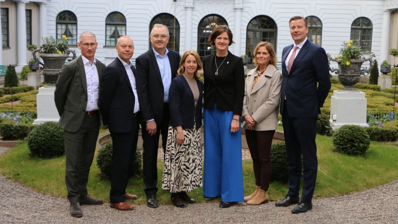 Sju personer framför en ståtlig trädgård