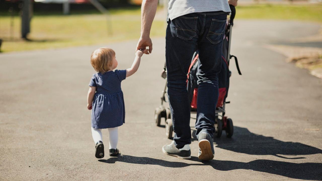 En pappar och barn går på promenad. Pappan håller barnet i handen.