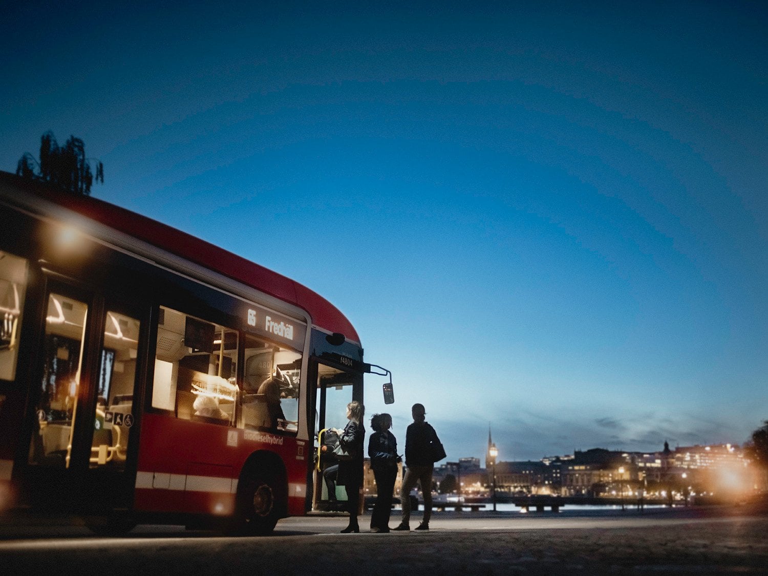 En rödbuss tar emot resenärer under skymning i Stockholm