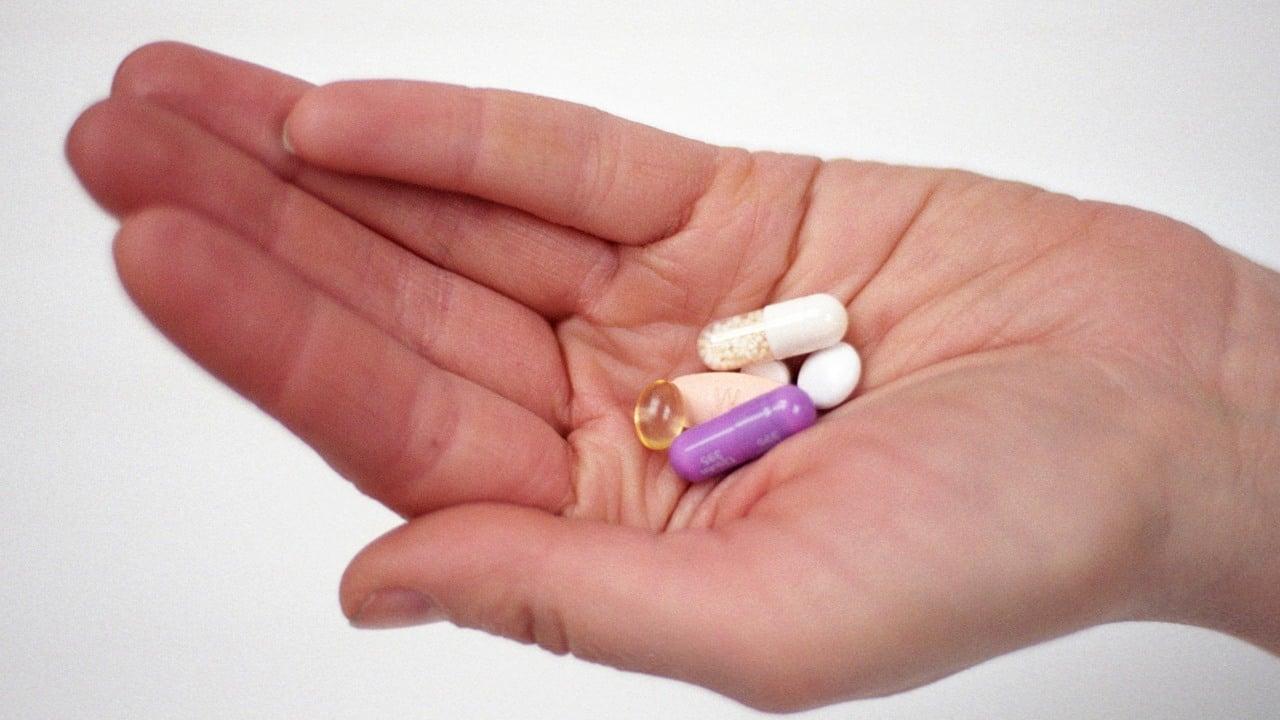 En hand som håller fram en liten hög med tabletter