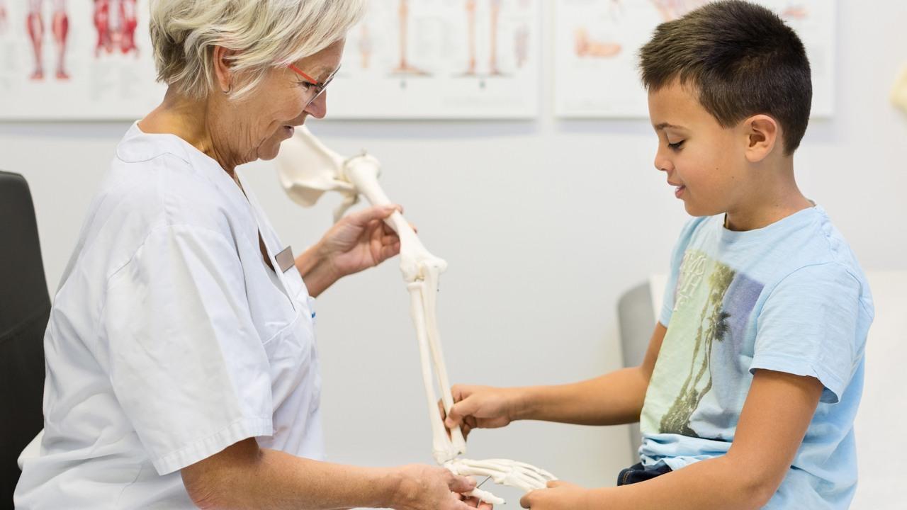 Kvinnlig vårdmedarbetare visar en pojke ca tio år ett skelett som ser ut att vara av ett människoben
