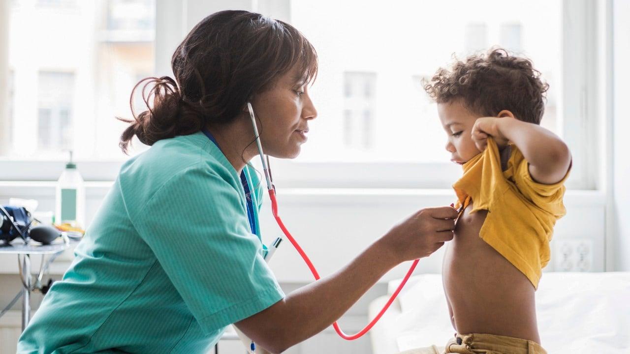 En kvinnlig vårdmedarbetare lyssnar på ett barns bröstkorg med ett stetoskop