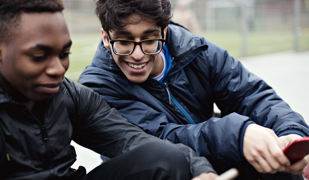Leende ung man tittar på vänners mobiltelefon.
