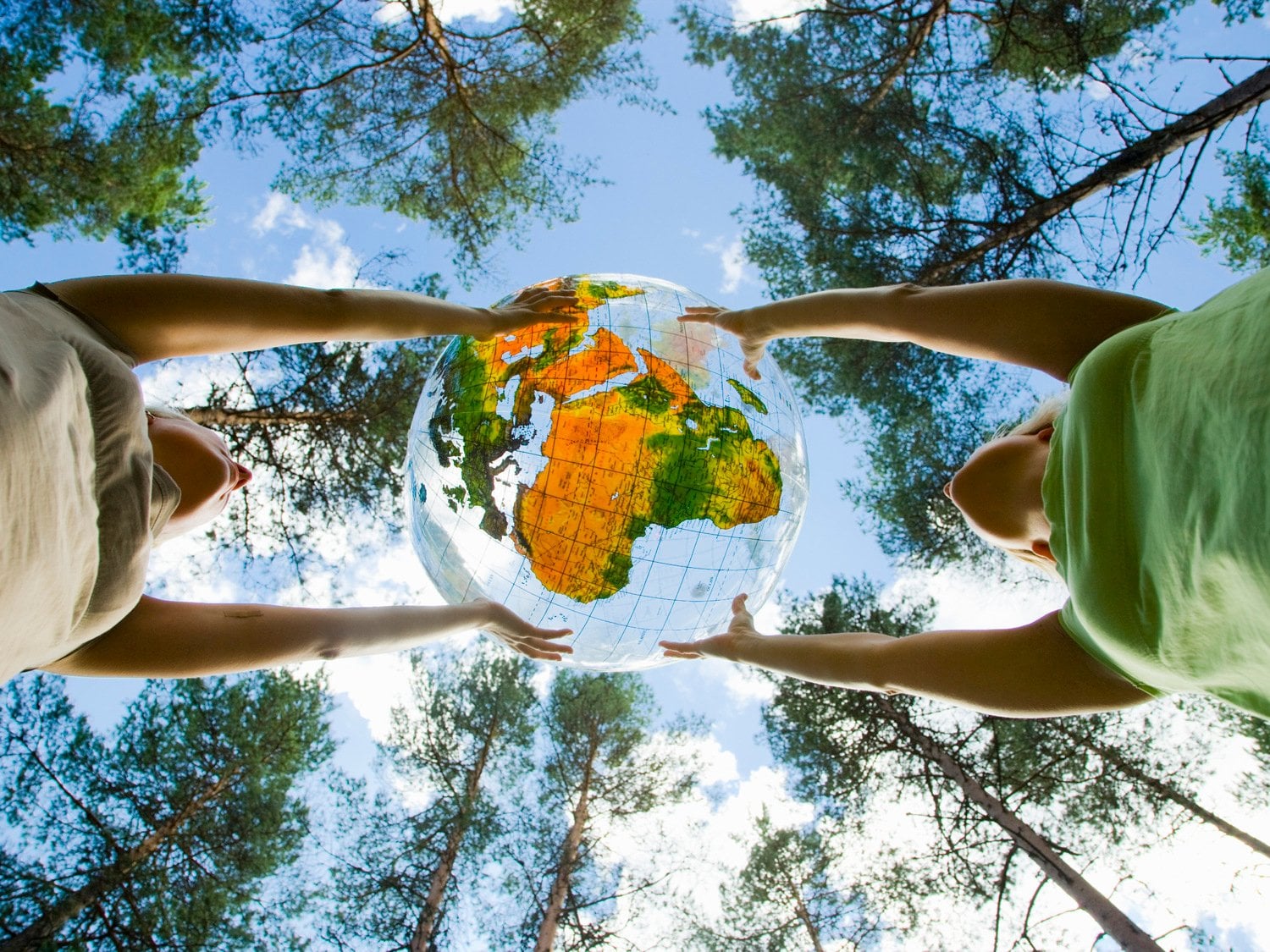 Två personer håller i en jordglob. Den syns underifrån och i bakgrunden syns stora gröna träd