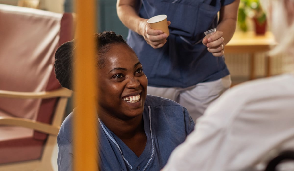 Foto på en vårdpersonal som sitter framför en patient och ler.