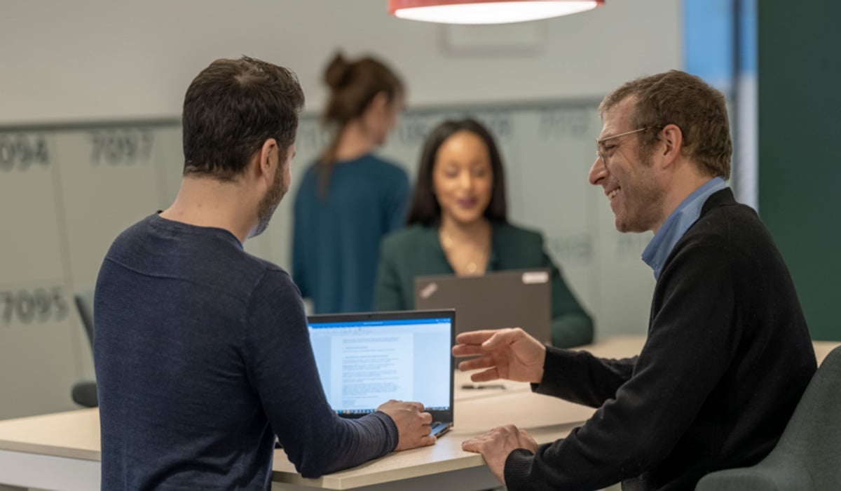 Foto på medarbetare som sitter vid datorer och pratar med varandra.