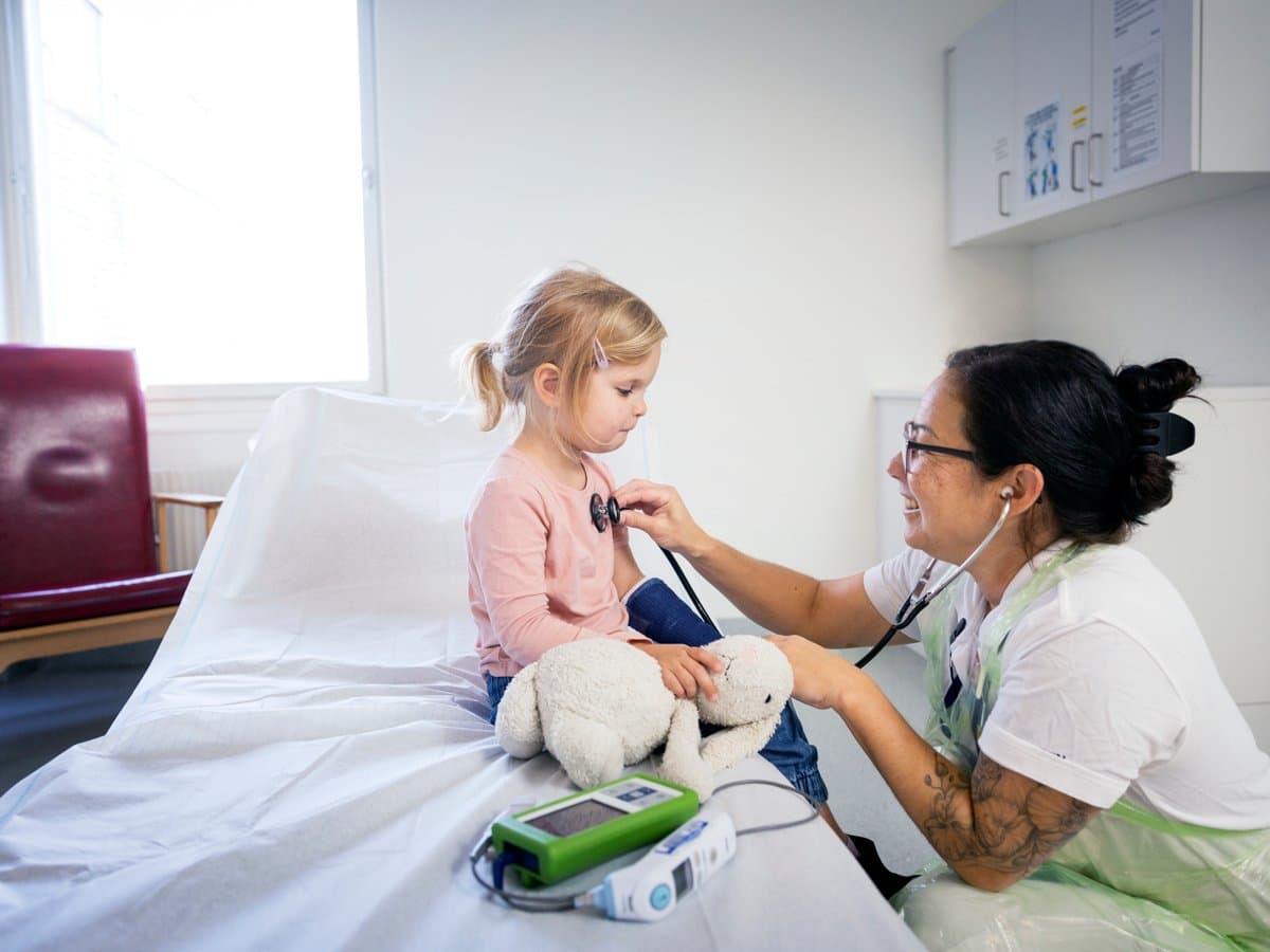 En liten flicka lyssnar på en läkares stetoskop.
