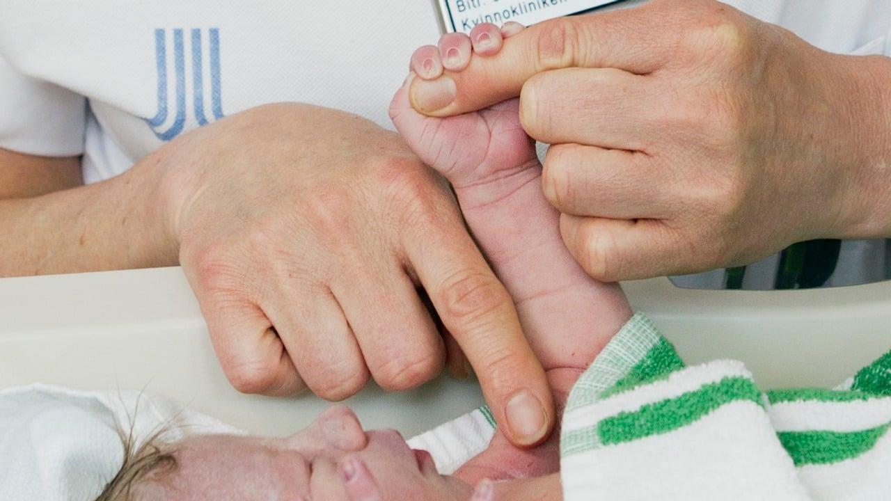 Nyfödd bebis med små händer håller i två större händer