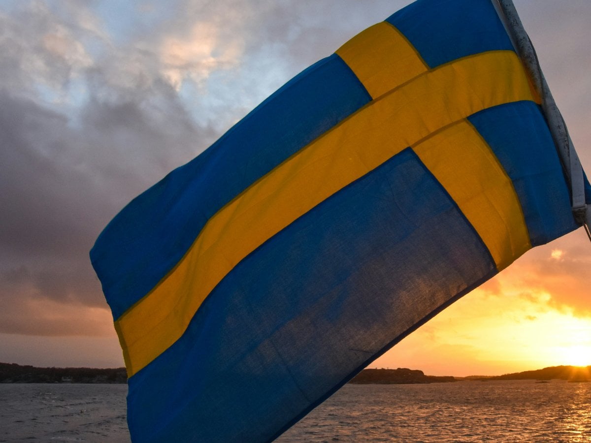 Svenska flaggan vajjar på en båt mot solnedgång.