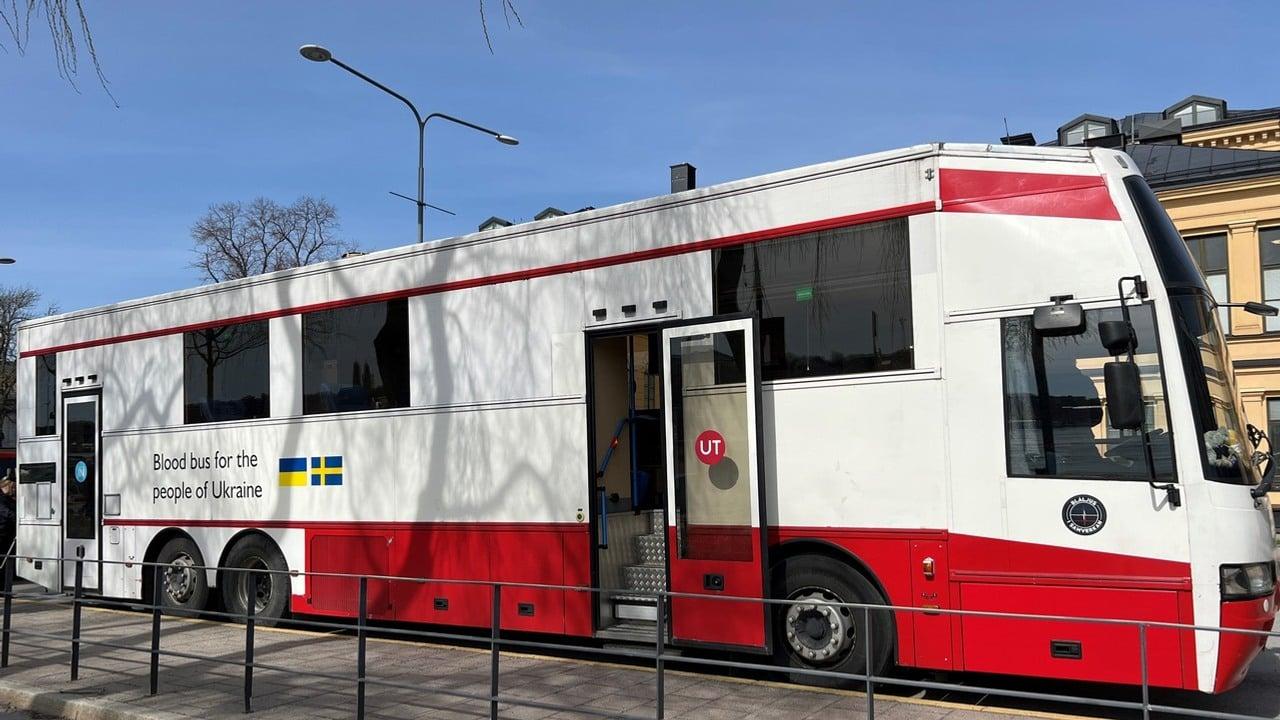 En stor vitröd buss som används som blodbuss. Den står parkerad med öppna dörrar.