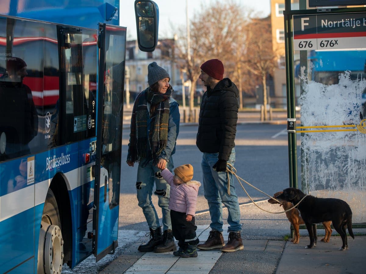 Kvinna med litet barn i handen, man och två hundar kliver på en buss