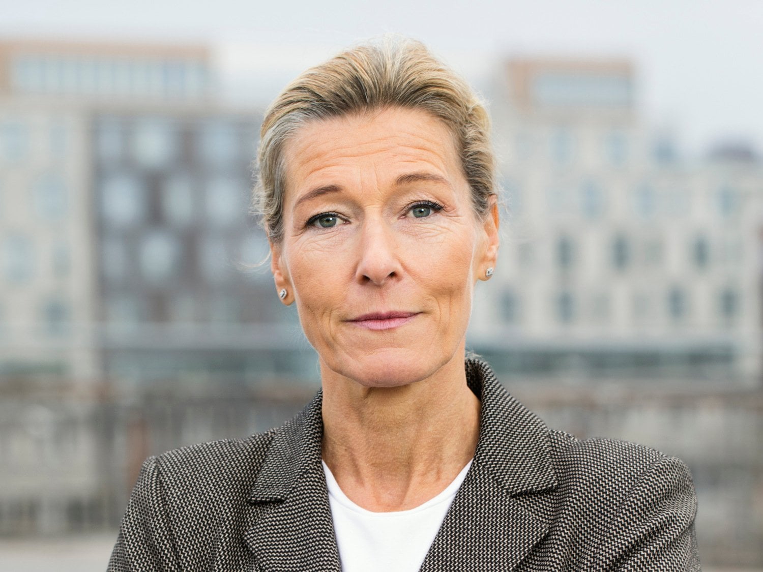 Kvinna tittar rakt in mot kameran. I bakgrunden syns gråa byggnader