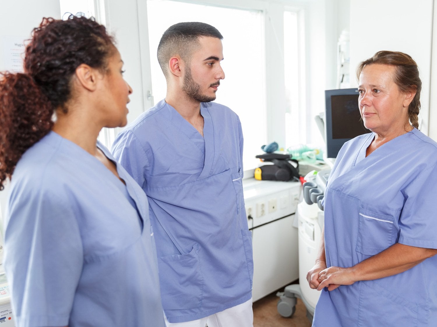 Tre medarbetare inom vården samtalar. De är klädda i blåa sjukhuskläder