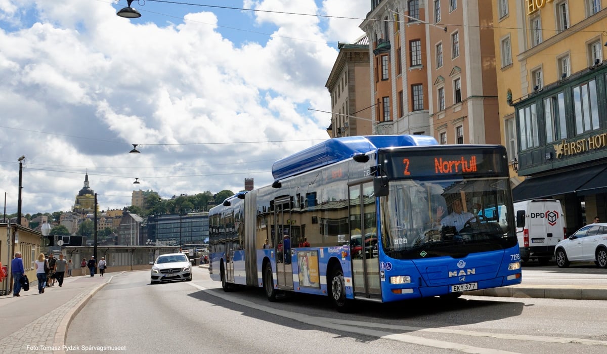 En blå stadsbuss åker förbi skeppsbron i ett soligt Stockholm