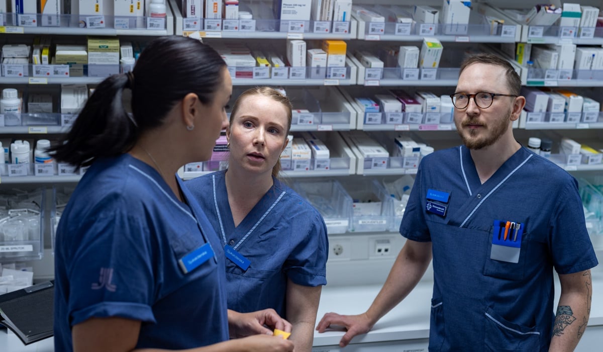 Tre personer i vårdkläder står och pratar med varandra.