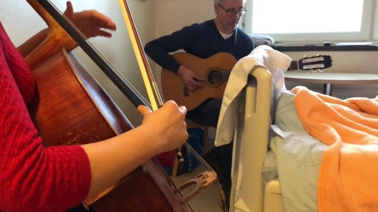 musiker framför sjuksäng spelar cello och gitarr
