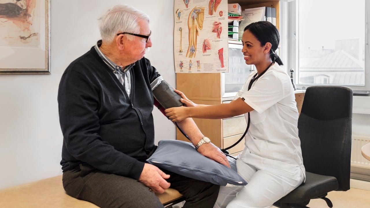 Kvinnlig vårdmedarbetare mäter blodtryck på en äldre manlig patient