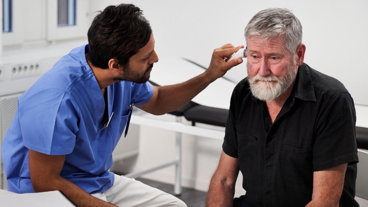 Manlig vårdmedarbetare håller en mätare av något slag i en manlig patients öra