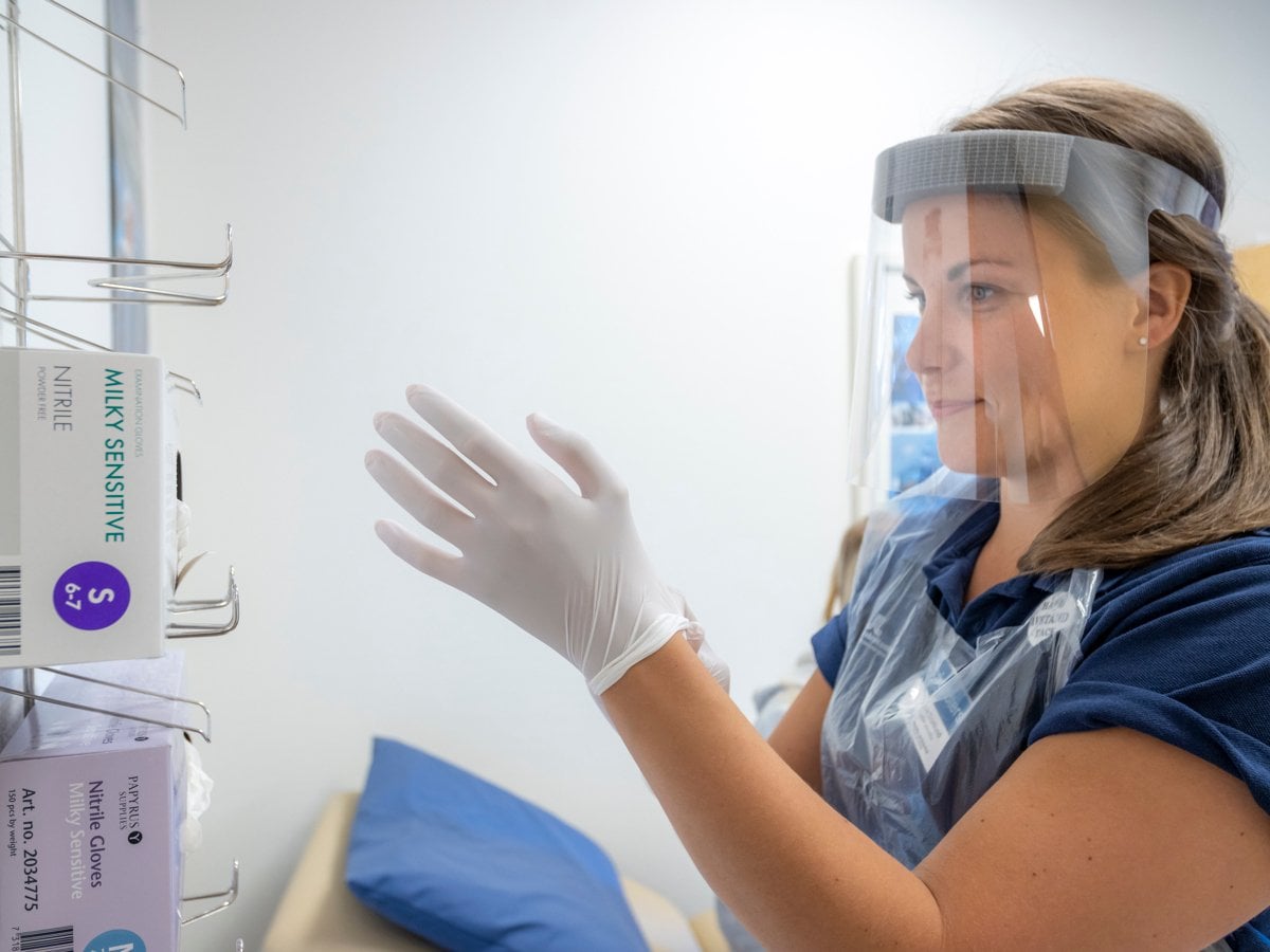 Kvinnlig vårdpersonal som sätter på sig vita plasthandskar