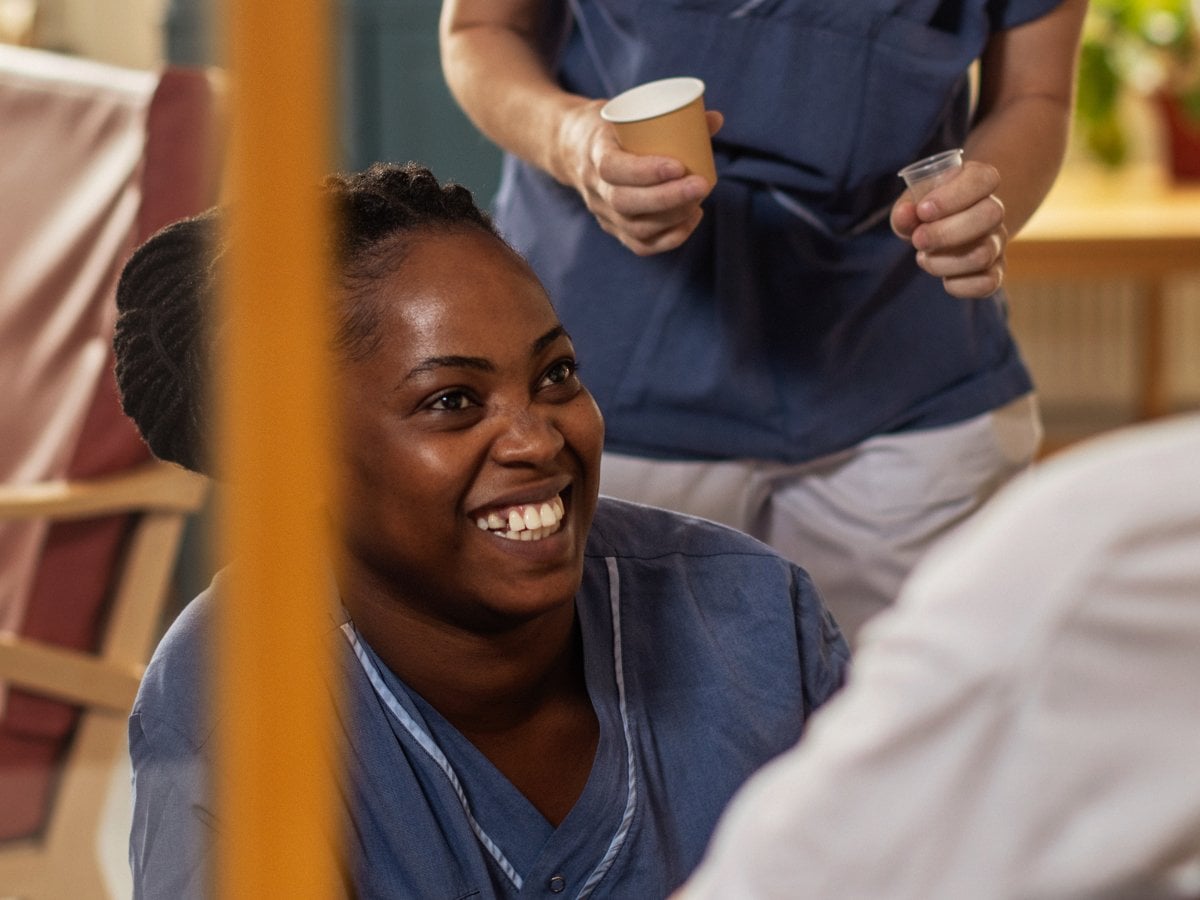 Ung undersköterska som sitter på huk framför en patient.
