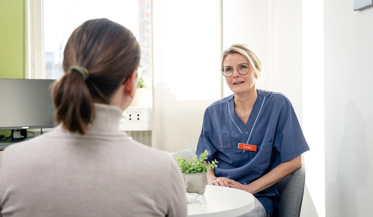 En kvinna sitter vid ett bord och pratar med en sjuksköterska.