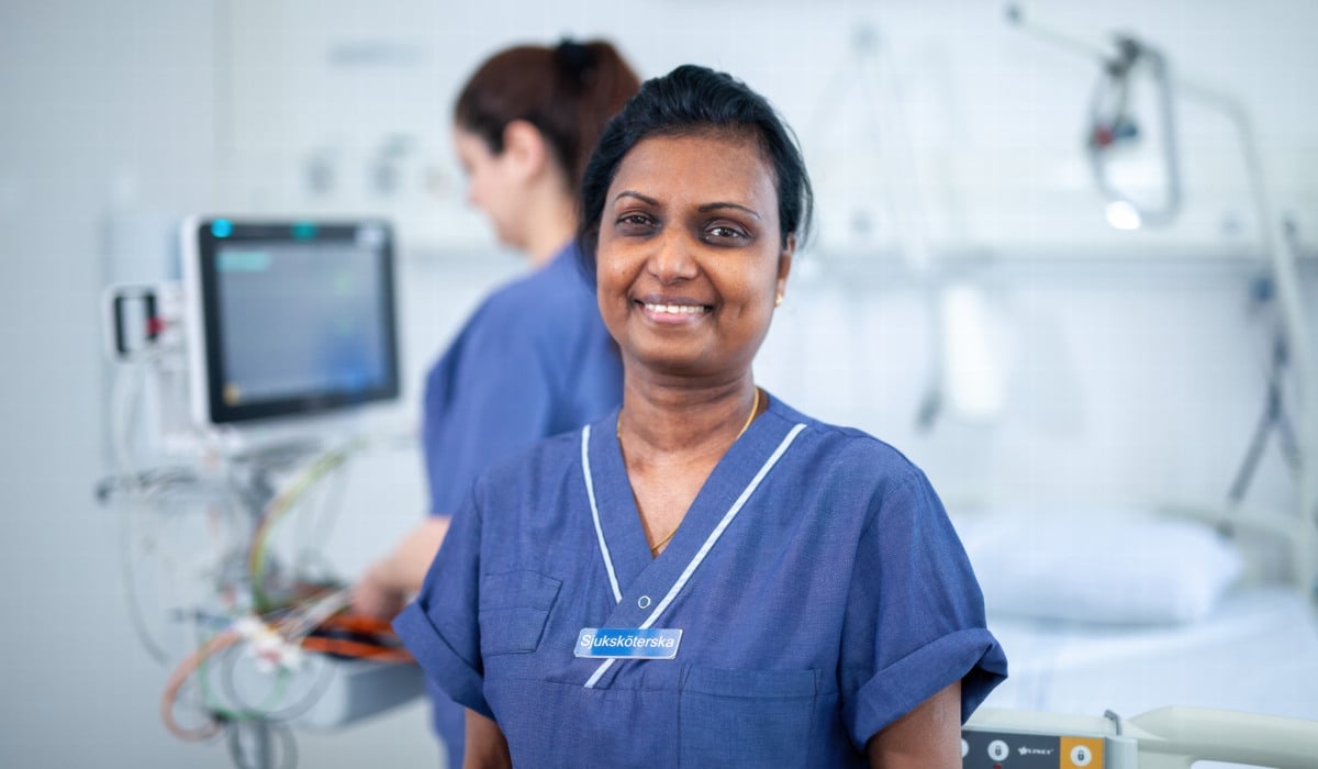 En kvinna i sjukhuskläder ler in i kameran.