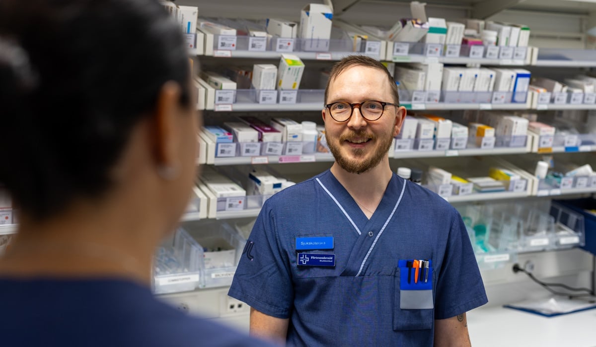 En man i sjukhuskläder står framför en hylla med läkemedel.